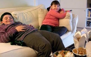 Overweight Brother and Sister Sitting on a Sofa Eating Takeaway Food and Watching the TV